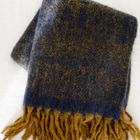 2: A fuzzy mohair-like blanket in navy and mustard with mustard tassel trim.
