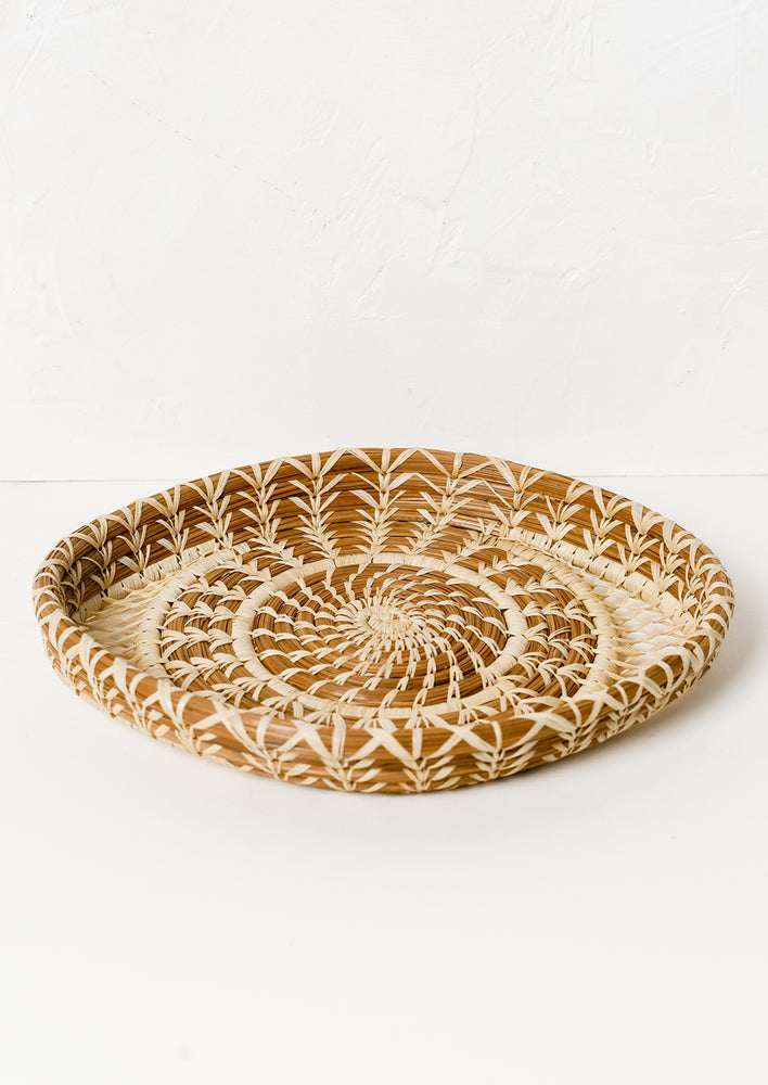 A shallow woven pine needle platter with raffia pattern detailing.
