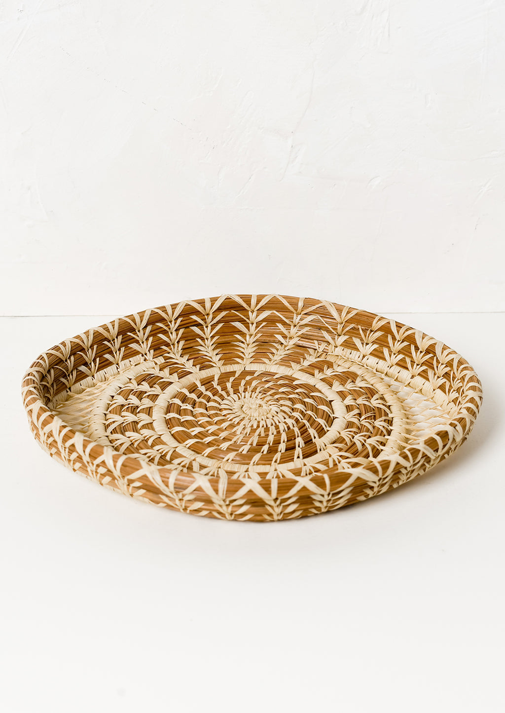 2: A shallow woven pine needle platter with raffia pattern detailing.
