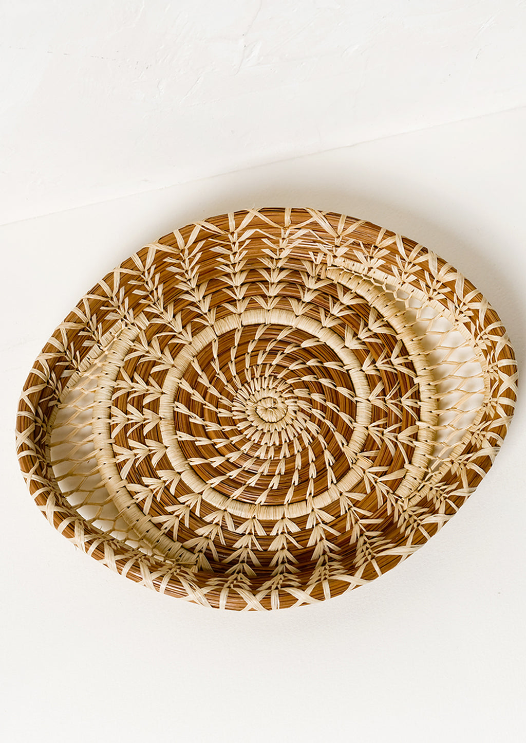 1: A shallow woven pine needle platter with raffia pattern detailing.