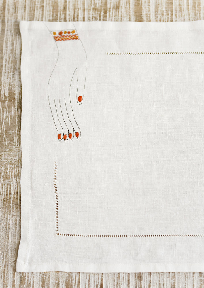 1: A white linen placemat with hemstitch border and embroidered hand at corner.