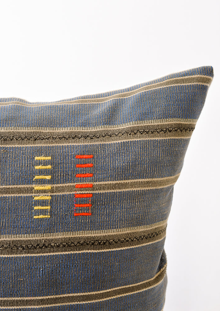 2: A detailed shot of an indigo and dark grey striped pillow, focusing on the yellow and red dash embroidery.