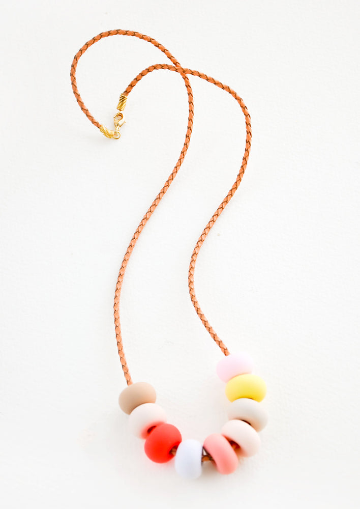 Woven leather cord necklace with gold clasp and rounded clay beads tans, pinks, red, blue, and yellow.