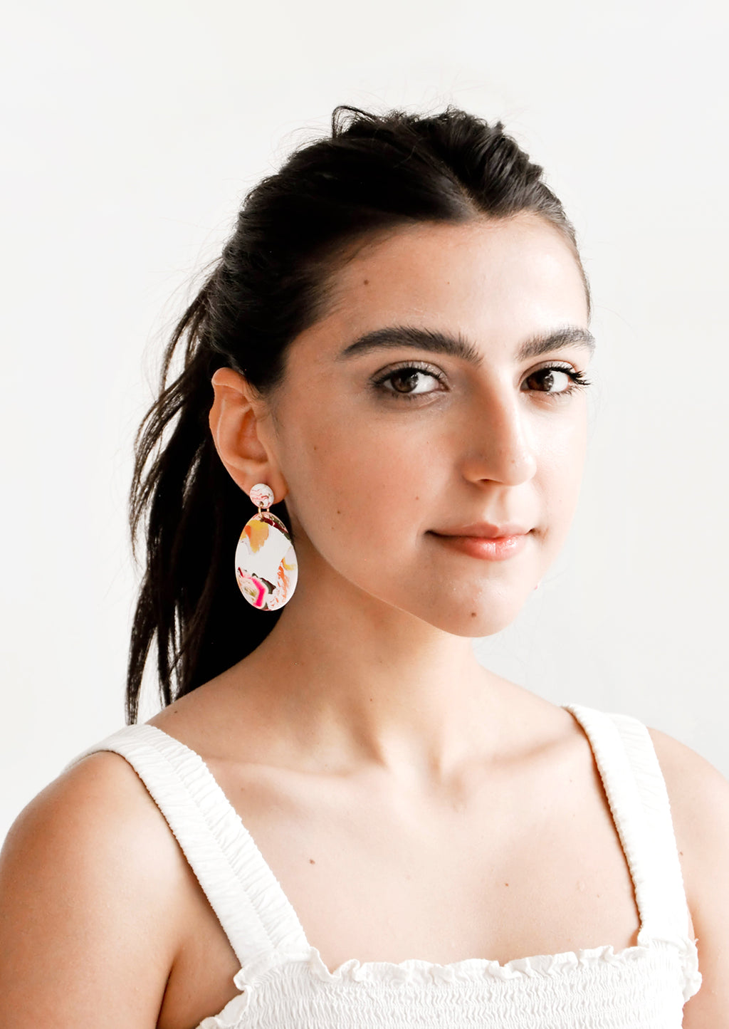 2: Model shot of woman wearing earrings and a white top.