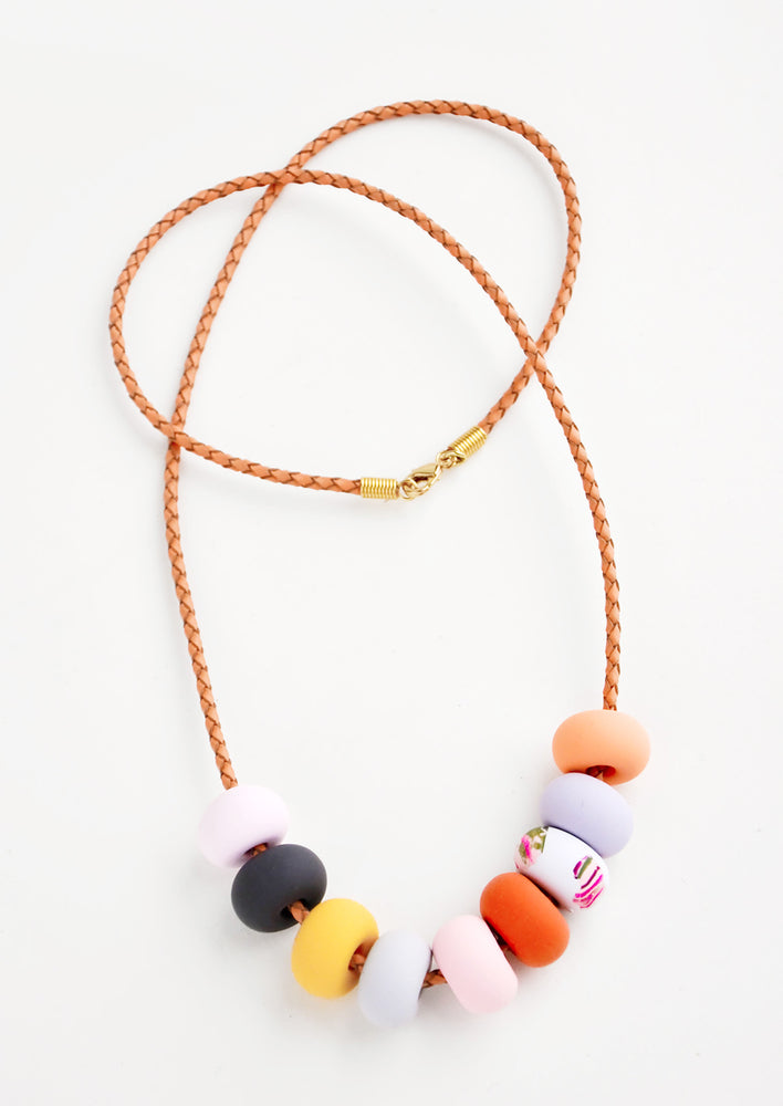 1: Necklace with light brown woven leather cord and nine clay beads in pink, navy, yellow, red, and orange.