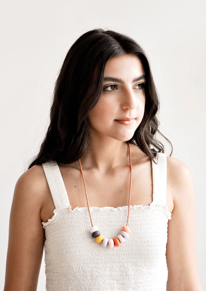 Model wears colorful clay bead necklace and white tank top.