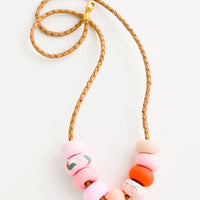 1: Necklace made from round clay beads in pink hues strung on braided leather cord