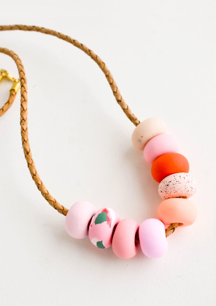 2: Round clay beads in pink, peach and red hues on leather cord