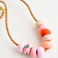 2: Round clay beads in pink, peach and red hues on leather cord