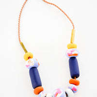 Big Bead: Necklace with gold clasp, brown woven leather cord, rectangular brass beads, and beads of varying shapes and sizes in yellows, pinks, blues, and oranges.