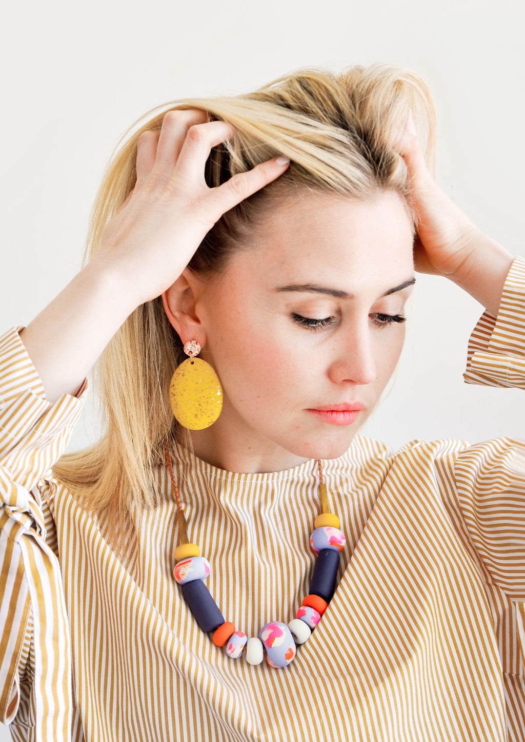 4: Model wears large yellow earrings and clay bead necklace. 