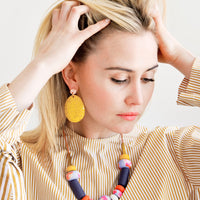 4: Model wears large yellow earrings and clay bead necklace. 