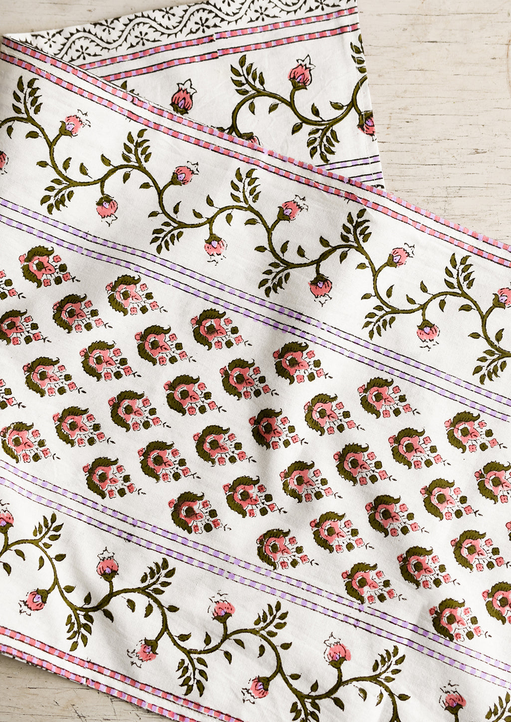 1: A block printed white table runner with pink, green and lavender floral print.