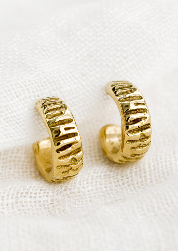 A pair of small brass hoop earrings with line texture.