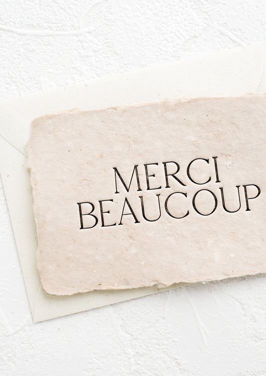 A greeting card made from blush handmade paper and large letters spelling "Merci Beaucoup".