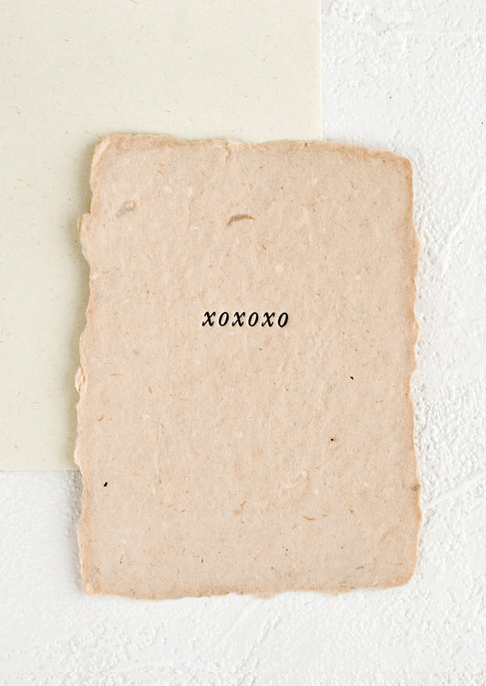 A greeting card made from pink handmade paper with "xoxoxo" printed on front.