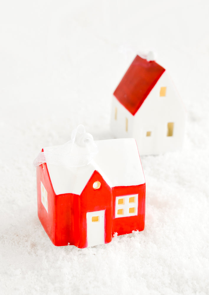 A ceramic christmas ornament in the shape of a farmhouse painted in red and white with interior lights.