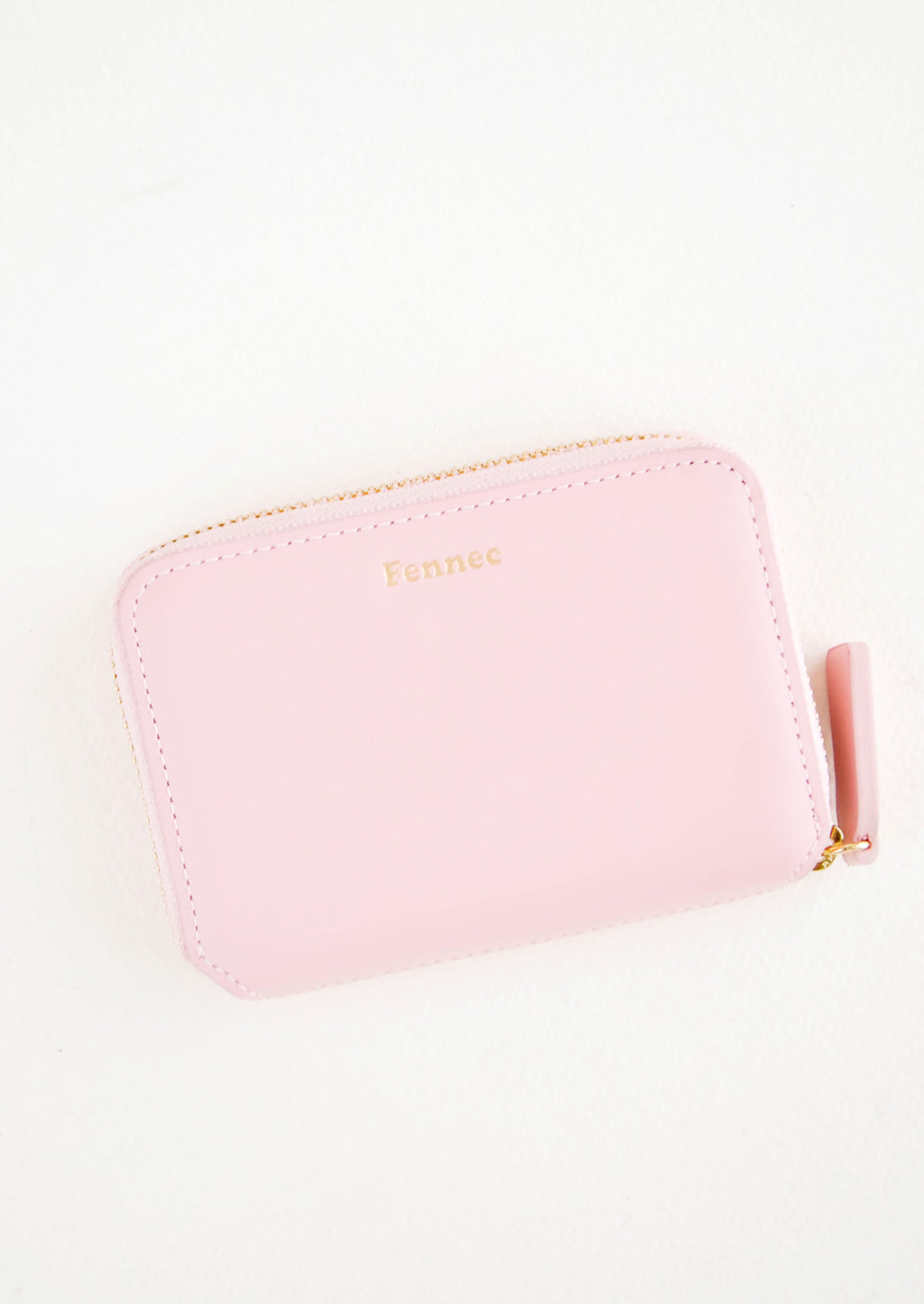 Pale Pink: Pale pink leather zip wallet with brand name Fennec embossed in small gold letters at top center of wallet face.