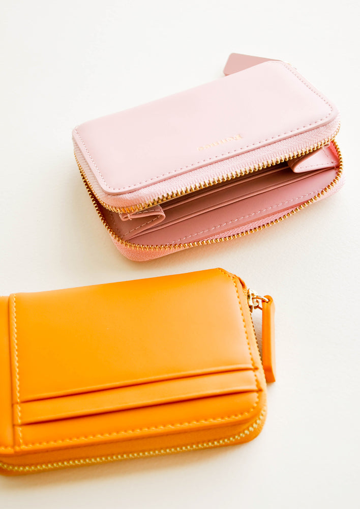 Pale pink leather wallet shown unzipped next to orange wallet with three exterior card slots.