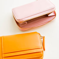 4: Pale pink leather wallet shown unzipped next to orange wallet with three exterior card slots.