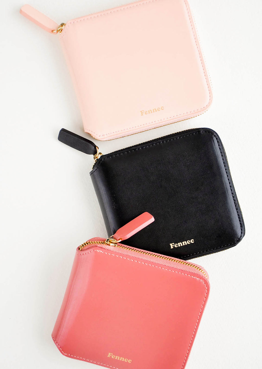 1: Three leather zip wallets in pale pink, black, and deep pink.