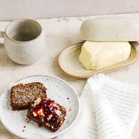 3: A breakfast tableware scene with coffee mug, butter dish and toast and jam on a ceramic plate.