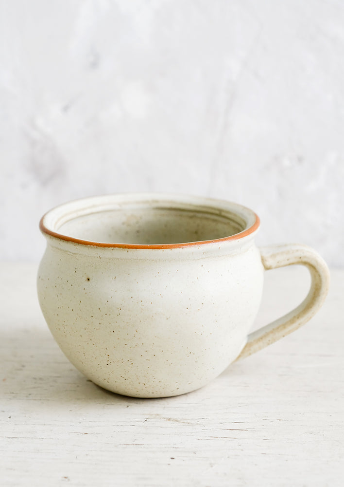 A beige ceramic mug with light speckling in a rounded shape with a handlle.