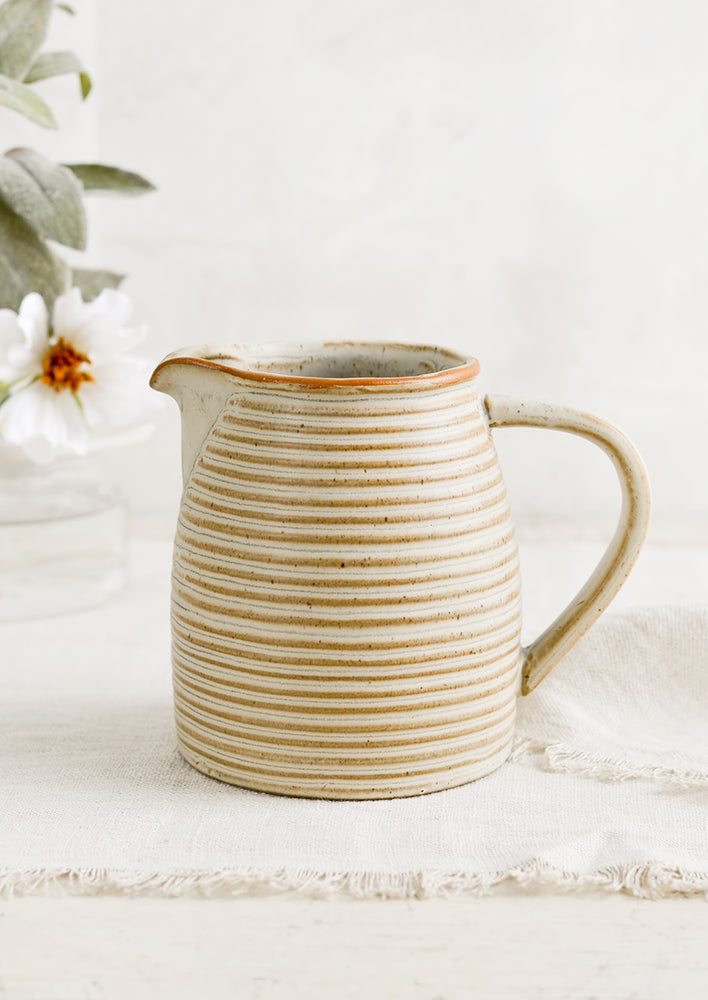 1: A tan ceramic pitcher with striped texture.