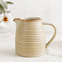 1: A tan ceramic pitcher with striped texture.