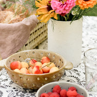 2: A vase with flowers on table with berry bowls.