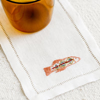 4: An white linen cocktail napkin with embroidered fish.