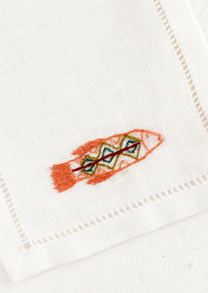 An white linen cocktail napkin with embroidered fish.