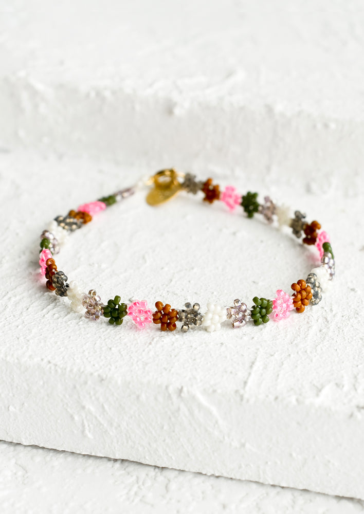 A beaded bracelet in flower shape in neon pink, olive, white and brown.