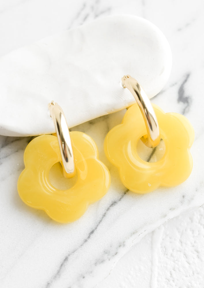 A pair of earrings with gold huggie hoop base and yellow flower charm.