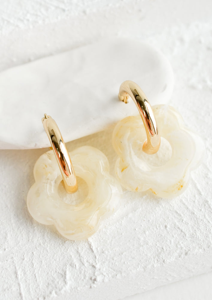 A pair of earrings with gold huggie hoop base and ivory flower charm.
