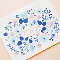 2: Greeting card with blue floral print frame around "Mom" printed in copper text