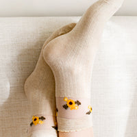 2: A pair of oatmeal colored socks with sheer mesh sunflower print band at ankle.
