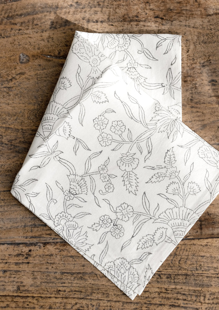 A cotton dinner napkin in white with gray floral outline print.