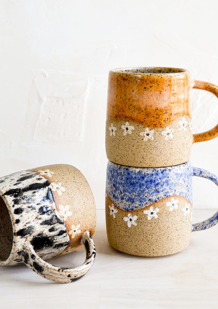 A stack of speckled ceramic coffee mugs with wavy daisy design.