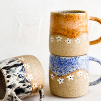 2: A stack of speckled ceramic coffee mugs with wavy daisy design.