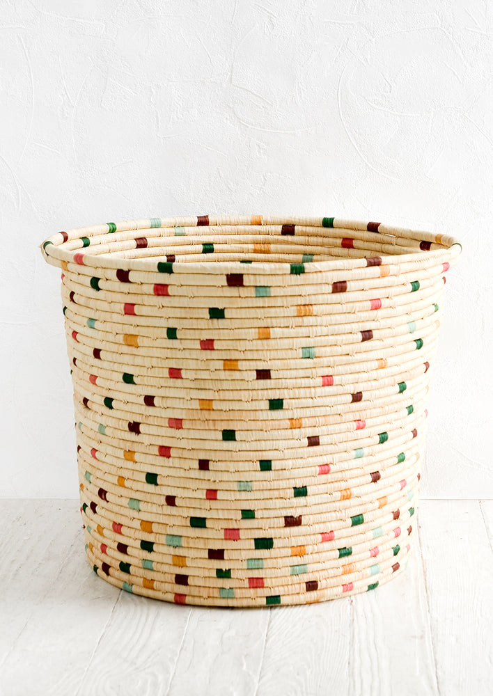 A round raffia hamper in natural with colorful dashes throughout.