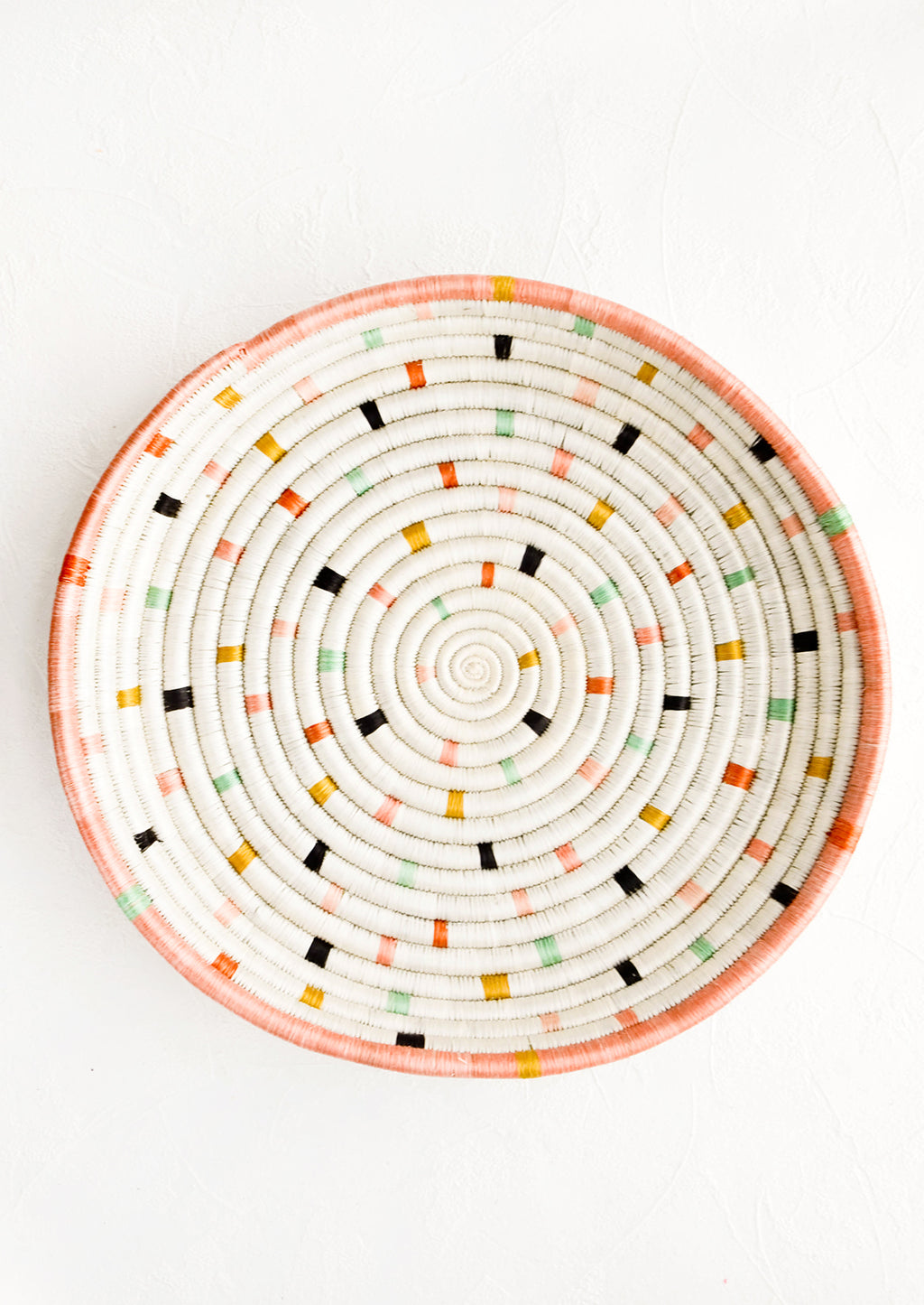 3: Round, shallow serving tray made from woven sweetgrass. Ivory with pastel colored dashes and peach rim.