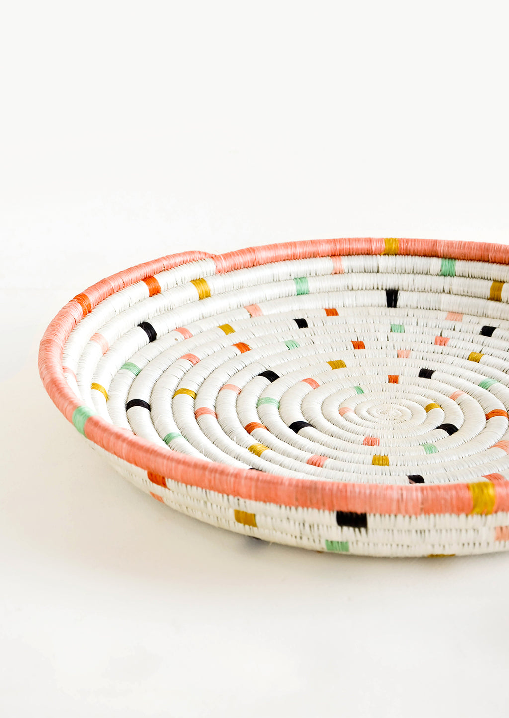 2: Round, shallow serving tray made from woven sweetgrass. Ivory with pastel colored dashes and peach rim.