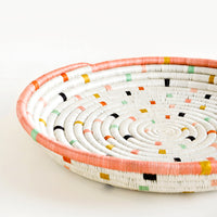 2: Round, shallow serving tray made from woven sweetgrass. Ivory with pastel colored dashes and peach rim.