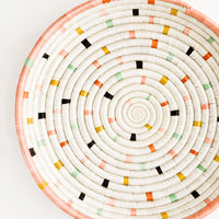 1: Round, shallow serving tray made from woven sweetgrass. Ivory with pastel colored dashes and peach rim.