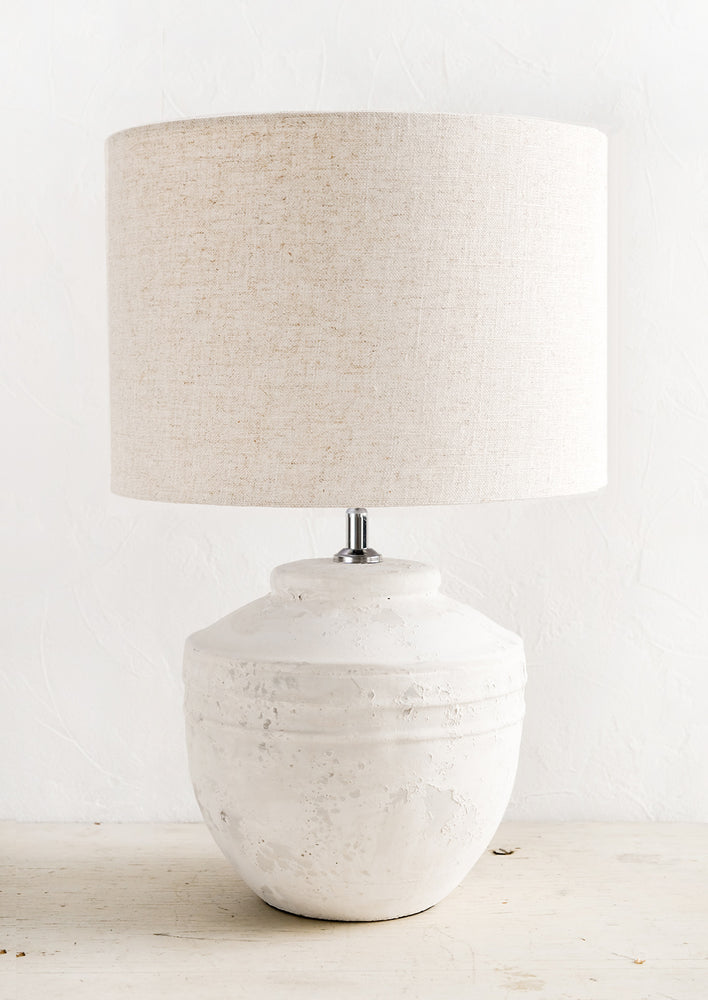 A white distressed concrete table lamp with a natural linen shade.