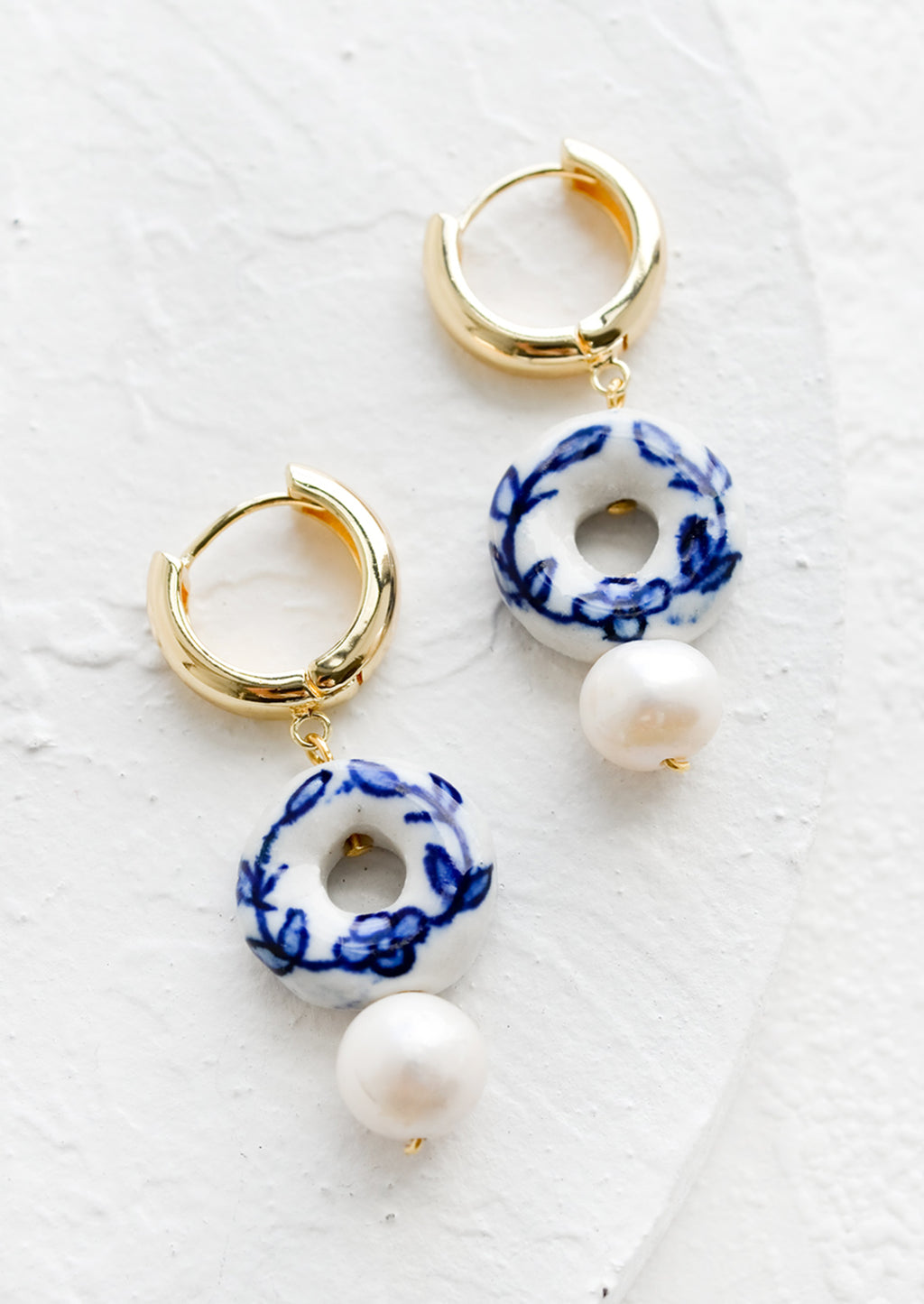 1: A pair of gold huggie hoops with donut shaped blue and white ceramic bead and pearl below.