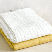 1: Quilted cotton throws in white and mustard, folded on a table