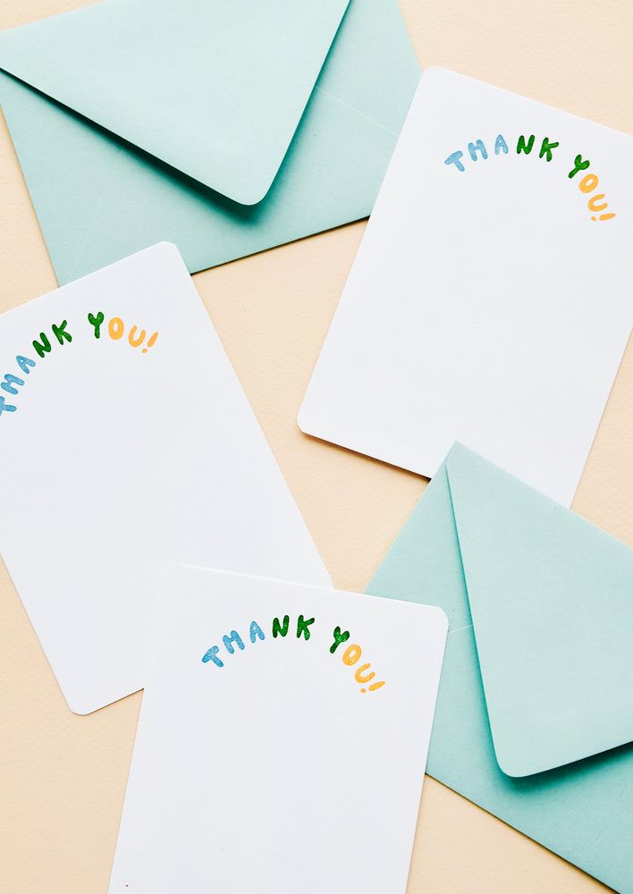 Multiple white notecards with "Thank you" in colorblocked, arc-shaped text at top, paired with turquoise envelopes.