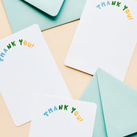 1: Multiple white notecards with "Thank you" in colorblocked, arc-shaped text at top, paired with turquoise envelopes.